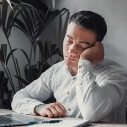 Image of man asleep at desk with head in hand